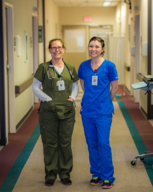 two healthcare workers stand in a hospital hallway